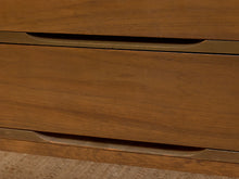 Load image into Gallery viewer, Close-up of a mid-century modern wooden dresser with warm brown wood grain and slim brass pull handles.