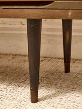 Load image into Gallery viewer, Close-up of the dark brown wooden legs of a vintage table resting on a textured beige woven rug against a white paneled wall.