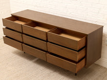 Load image into Gallery viewer, A mid-century modern wooden dresser with nine drawers, including all nine open drawers, shown against a white brick wall and beige carpet.