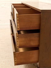 Load image into Gallery viewer, Close-up of a wooden dresser with three drawers pulled open, showing the warm medium-brown wood grain and dovetail joint construction, set against a light neutral background.