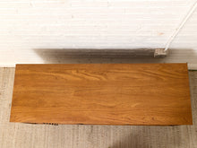 Load image into Gallery viewer, A rectangular wooden coffee table with a warm medium-brown wood grain finish, photographed from above against a white brick wall and beige woven rug.