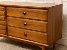 Load image into Gallery viewer, Mid-century modern wooden dresser with three drawers featuring round brass pulls, set against a white brick wall and textured carpet.