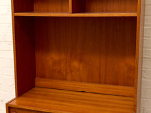 Load image into Gallery viewer, Close-up of the interior of a wooden bookcase or shelving unit with warm medium-brown wood grain and open compartments, photographed against a white painted brick wall.