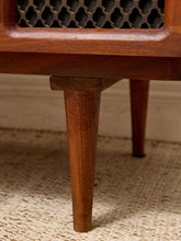 Load image into Gallery viewer, Close-up of a mid-century modern wooden sideboard or cabinet leg, showcasing the warm brown wood grain, a decorative metal lattice screen, and a woven beige rug underneath.