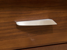 Load image into Gallery viewer, A brushed silver metal drawer pull handle mounted on a dark brown wood-grained cabinet door.