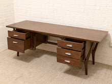 Load image into Gallery viewer, Mid-century modern wooden writing desk with a dark walnut finish, featuring three open drawers on the left, three open drawers on the right, and a drop-down center panel. The desk is shown with its drawers open, set against a white brick wall and beige carpet.