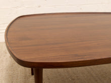 Load image into Gallery viewer, Close-up of a mid-century modern wooden coffee table with a rounded rectangular top and warm brown wood grain, set against a white brick wall and beige rug.