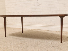 Load image into Gallery viewer, A mid-century modern wooden console table with tapered legs, shown on a textured beige rug against a white brick wall.