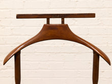 Load image into Gallery viewer, A vintage wooden hanger with a polished finish, featuring a flat top bar and curved legs, set against a white painted brick wall.