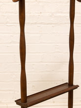 Load image into Gallery viewer, A close-up of a dark brown wooden coat rack with twisted vertical posts and a lower shelf, set against a white painted brick wall.