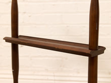 Load image into Gallery viewer, A close-up of a dark brown wooden shelf or rack with two vertical posts, set against a light beige painted brick wall.
