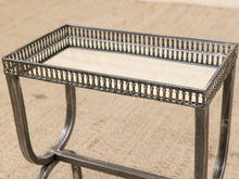 Load image into Gallery viewer, A rectangular metal side table with a mirrored glass top and an ornate openwork balustrade-style border, shown on a beige textured rug.