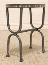 Load image into Gallery viewer, A vintage industrial-style metal side table with a textured, perforated rectangular top and four curved legs, shown on a woven rug against a light brick wall.