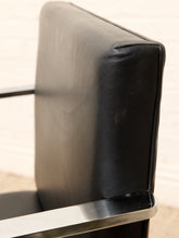 Load image into Gallery viewer, Close-up of a black leather upholstered chair back with a polished metal armrest and trim, photographed outdoors against a light neutral background.