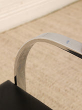 Load image into Gallery viewer, Close-up detail of a curved metallic chair armrest in polished silver, resting against a beige carpeted floor.