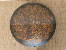 Load image into Gallery viewer, A round decorative tray or plate featuring a vintage-style floral pattern in mottled brown, gold, and black tones, set against a textured beige woven background.