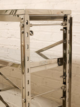 Load image into Gallery viewer, A close-up of a polished stainless steel shelving unit with adjustable metal brackets, set against a white painted brick wall.