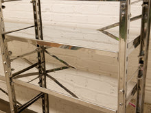 Load image into Gallery viewer, A close-up of a polished stainless steel industrial shelving unit with multiple tiers, set against a white painted brick wall.
