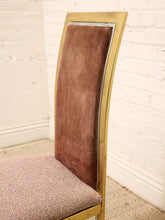 Load image into Gallery viewer, A close-up of a modern dining chair featuring a curved backrest upholstered in brown velvet, a textured beige seat cushion, and a polished gold metal frame, set against a white brick wall.