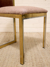 Load image into Gallery viewer, A close-up of a mid-century modern dining chair featuring a textured mauve-pink upholstered seat cushion and a polished brass frame, set on a woven jute rug against a white brick wall.