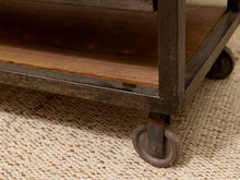 Load image into Gallery viewer, Close-up of a rustic industrial rolling storage cart with a dark metal frame, wooden shelves, and casters on a woven beige rug.