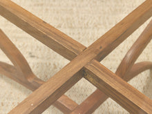 Load image into Gallery viewer, Close-up detail of a wooden furniture base with crossed legs and a woven beige rug underneath.