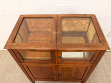 Load image into Gallery viewer, A mid-century wooden display cabinet with a warm brown finish, featuring two upper glass-front compartments and two lower doors, set against a white brick wall and light-colored carpet.