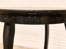 Load image into Gallery viewer, Close-up of a black wooden table leg and apron with a distressed finish and a faded floral pattern, set against a light off-white paneled background.