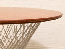 Load image into Gallery viewer, Close-up of a round wooden table top with a warm medium-brown finish and visible wood grain, supported by a white wire chair-style base against a white brick wall background.
