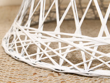 Load image into Gallery viewer, Close-up of a white woven wicker chair base or stool leg resting on a textured beige woven rug.