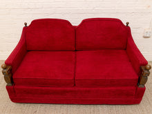 Load image into Gallery viewer, A vintage red upholstered loveseat with dark wood armrests and ball finials, set against a white brick wall.