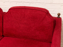Load image into Gallery viewer, A close-up of a red upholstered armchair or sofa section with a tufted backrest, red seat cushion, and a dark wooden finial on the arm, set against a white painted brick wall.