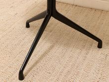 Load image into Gallery viewer, Close-up of a glossy black metal table base with three legs, shown on a textured beige woven rug.