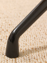 Load image into Gallery viewer, Close-up of a black metal chair leg with a tapered base resting on a woven beige rug.