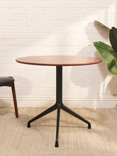 Load image into Gallery viewer, Round walnut-tone dining table with wood top and black three-prong metal pedestal base