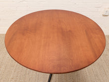 Load image into Gallery viewer, A round wooden table top with a warm medium-brown finish and visible wood grain, photographed indoors against a white brick wall and light rug.