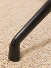 Load image into Gallery viewer, Close-up of a black metal chair leg with a curved foot, resting on a woven beige jute or sisal rug.