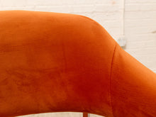 Load image into Gallery viewer, Close-up of a curved orange upholstered surface, likely part of a chair or bench, with a white brick wall background.