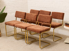 Load image into Gallery viewer, Six matching mid-century modern dining chairs with rust-brown corduroy upholstery and gold metal cantilever frames, arranged in two rows against a white brick wall.