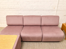 Load image into Gallery viewer, A three-seat modular sofa upholstered in dusty rose pink velvet, positioned against a white brick wall on a textured beige carpet.