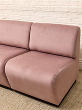 Load image into Gallery viewer, A dusty pink velvet two-seater sofa with rounded edges, shown against a white brick wall and light beige woven rug.