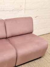 Load image into Gallery viewer, A close-up of a dusty pink velvet modular sofa corner against a white brick wall and textured beige carpet.