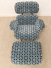 Load image into Gallery viewer, A three-piece lounge chair set with an armchair, matching ottoman, and a tall matching backrest, upholstered in a black fabric with a white geometric interlocking pattern, set on a beige woven rug against a white paneled wall.