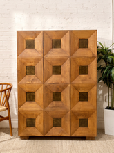 Load image into Gallery viewer, Vintage tall wood armoire with sculptural geometric panel doors, square dark wood-tone insets, and warm natural wood grain.