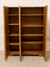 Load image into Gallery viewer, A tall wooden bookcase with two doors open, showing five shelves inside, set against a white brick wall and light beige carpet.