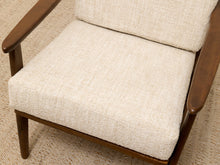 Load image into Gallery viewer, Close-up of a mid-century modern armchair with textured cream bouclé seat and back cushions and a dark brown wooden frame, set on a woven jute rug.