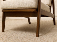 Load image into Gallery viewer, Close-up of a mid-century modern armchair showing the dark brown wooden frame, textured cream bouclé seat cushion, and woven beige rug underneath.