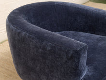 Load image into Gallery viewer, Close-up of a curved upholstered armchair in dark navy blue velvet fabric, showing the soft texture and rounded silhouette.