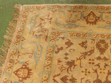 Load image into Gallery viewer, A close-up of a vintage-style area rug with a warm beige base, featuring brown and muted blue geometric and animal motifs, with fringed edges visible on the left.