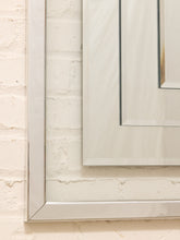 Load image into Gallery viewer, A close-up of a large rectangular mirror with a thick, polished silver frame mounted on a white painted brick wall.